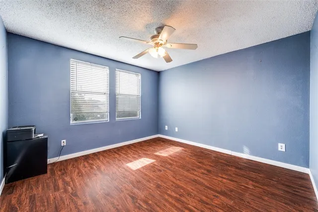 an empty room with wooden floor fan and windows