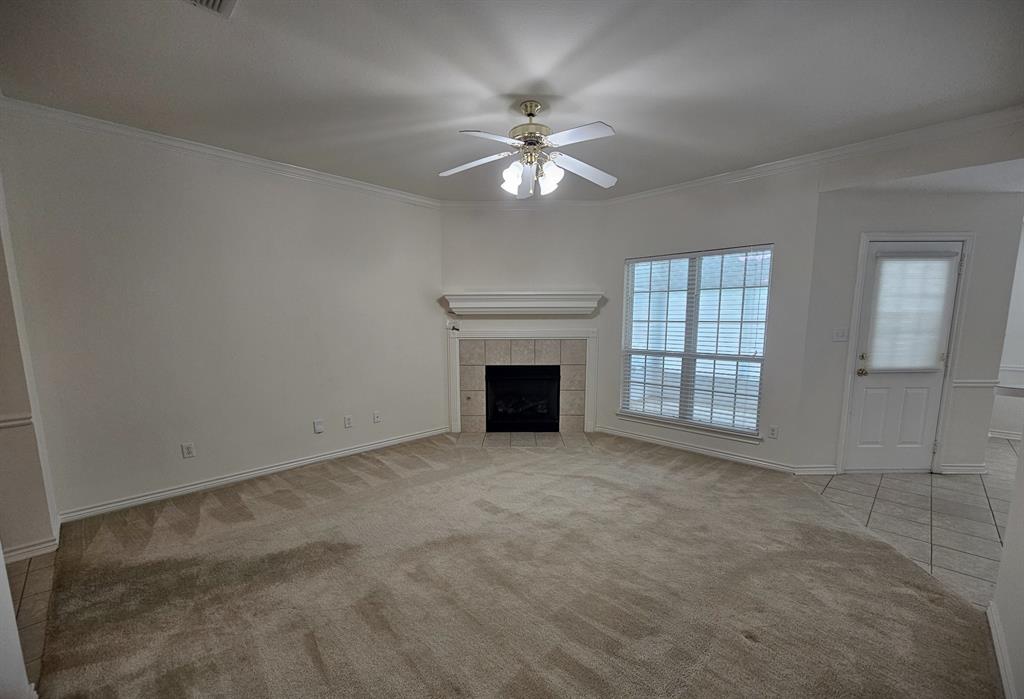 Spacious living area featuring a fireplace with a tile surround and mantel, a ceiling fan with integrated lighting, and multiple windows