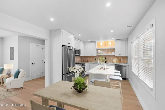 a room with stainless steel appliances kitchen island granite countertop a refrigerator a sink a dining table and chairs