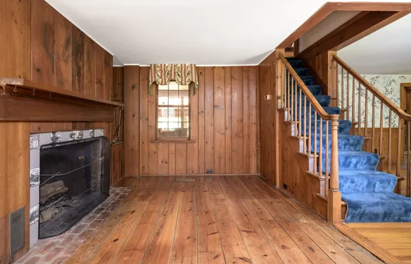a view of an empty room with wooden floor fireplace and a window
