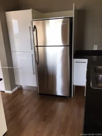 a view of a refrigerator in kitchen and an empty room with wooden floor