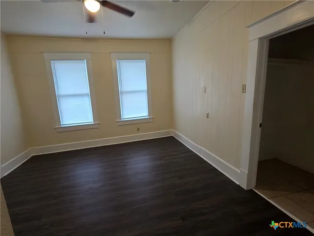 an empty room with wooden floor cabinet and windows