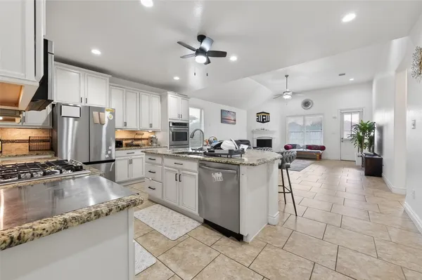 a kitchen with stainless steel appliances granite countertop a refrigerator oven a sink dishwasher and white cabinets with wooden floor