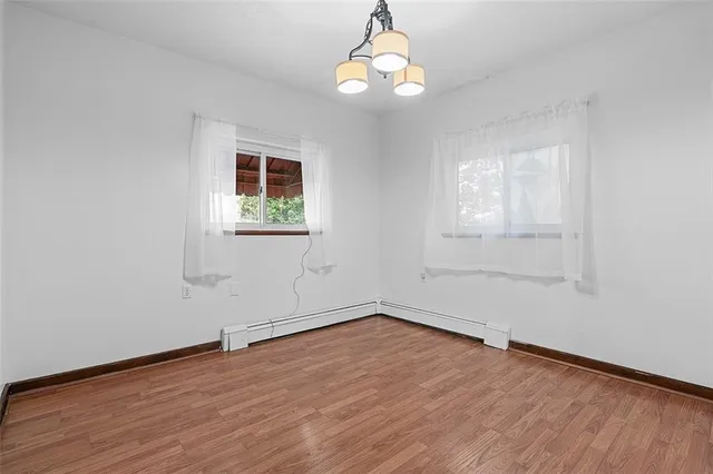 an empty room with wooden floor exposed radiator and windows
