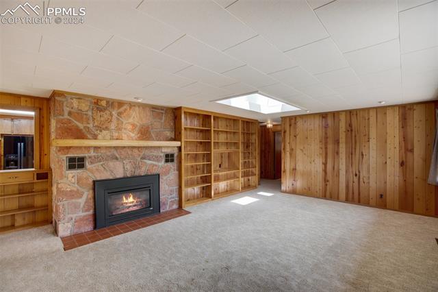 4980 Dodd Road Cascade, CO 80809 - Photo 17 of 48 Living room with carpet, a fireplace, a skylight, built in bookcases, and wooden walls