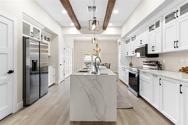 a large kitchen with stainless steel appliances a refrigerator a stove a sink dishwasher a oven with white cabinets and wooden floor