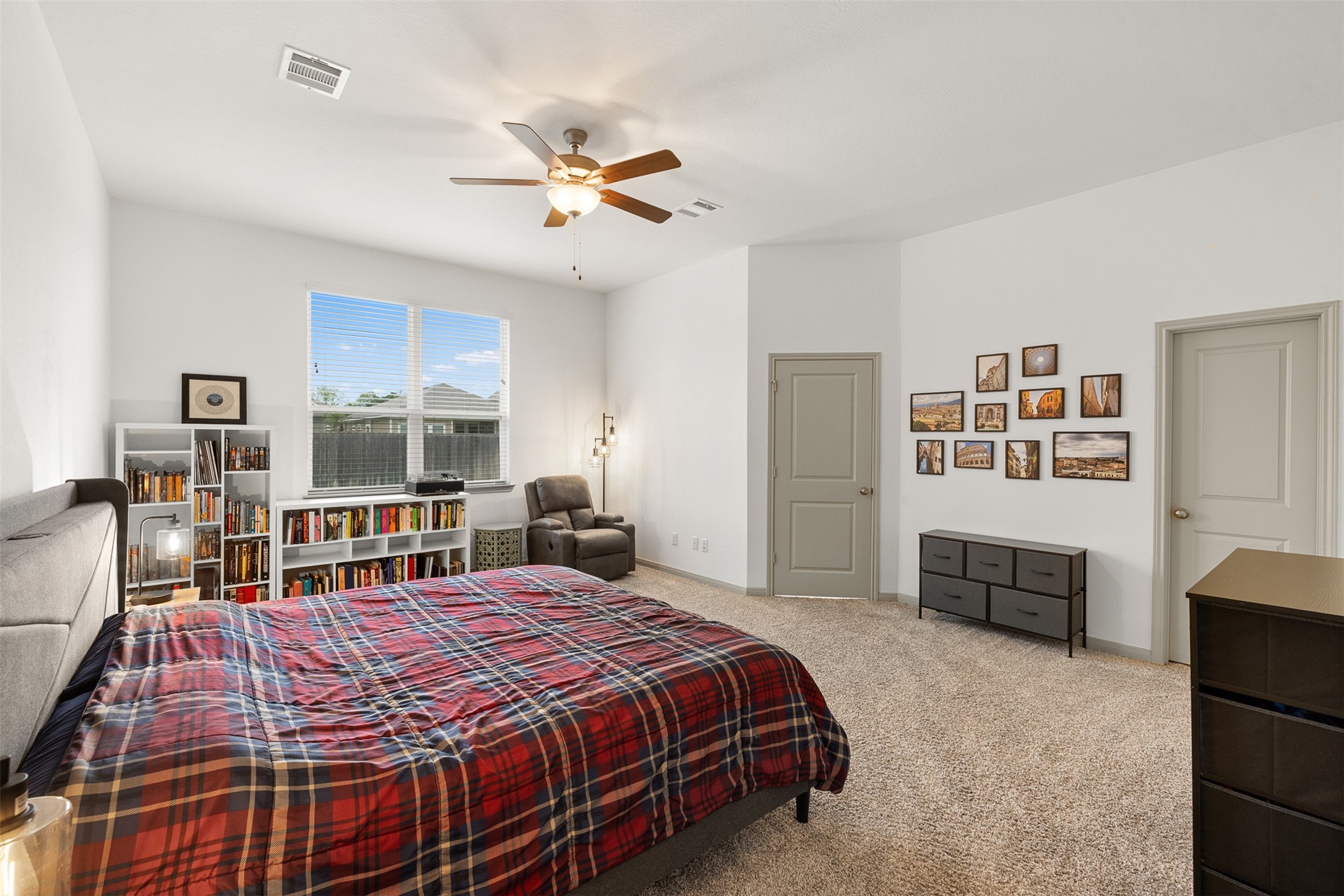 1968 Chief Street Bryan, TX 77807 - Photo 6 of 27 Spacious bedroom with neutral walls and carpet, featuring a large window for natural light. It includes a ceiling fan, a cozy reading nook with bookshelves, offering a comfortable and inviting atmosphere.
