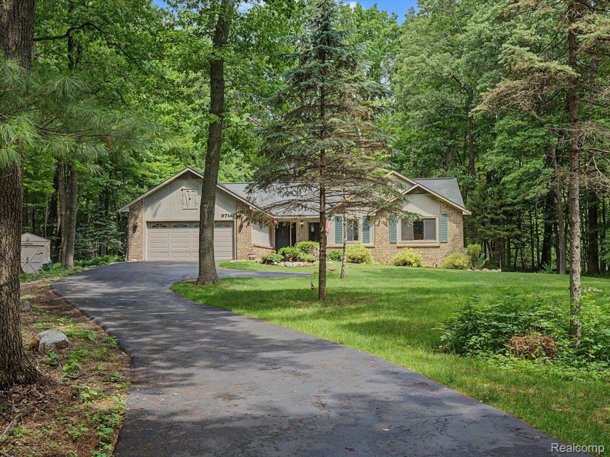 9714 Naiad Road Clarkston, MI 48348 - Photo 3 of 61 Ranch-style home showcasing a brick facade with shuttered windows, a two-car attached garage, and an asphalt driveway that curves gracefully as it leads to the front entrance.