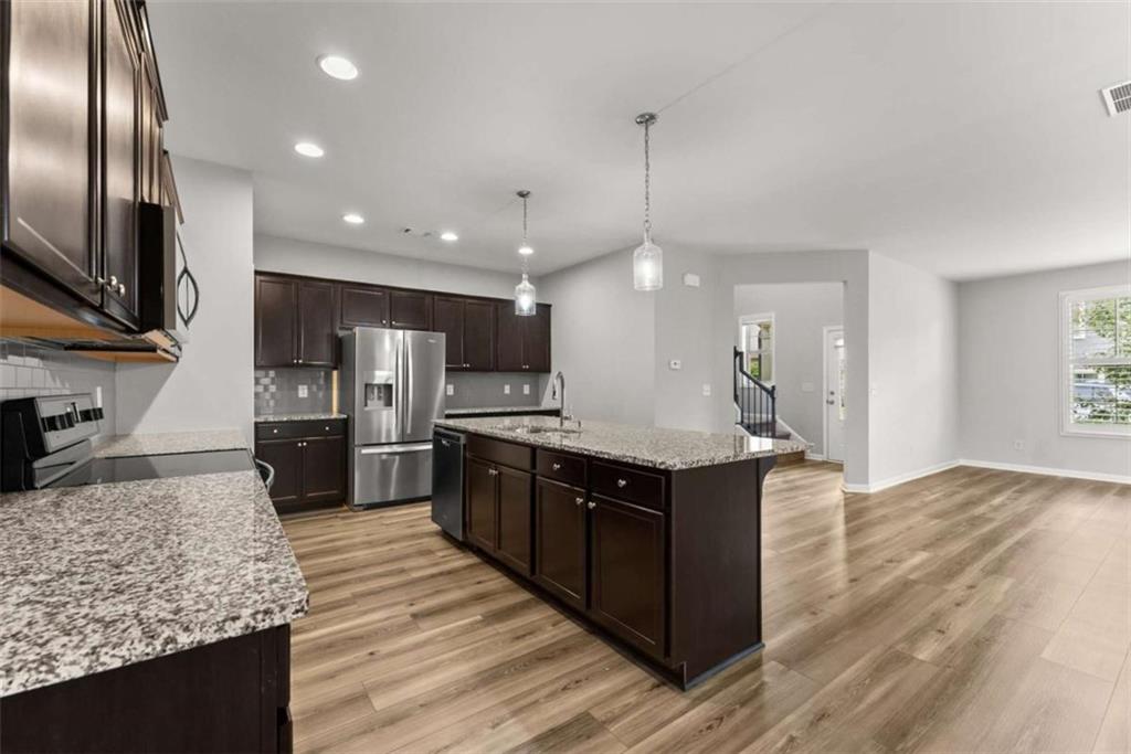 6021 Harbour Mist Drive Flowery Branch, GA 30542 - Photo 12 of 36 a large kitchen with stainless steel appliances kitchen island granite countertop a large counter top and wooden floors