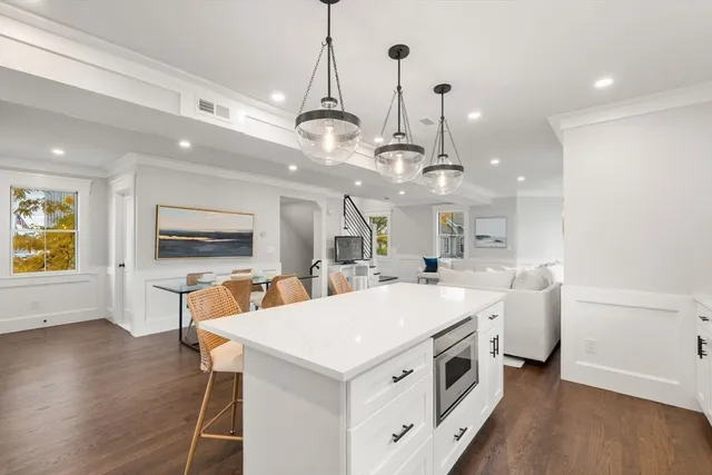 a large white kitchen with a stove a sink dishwasher a dining table and chairs with wooden floor