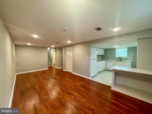 a view of an empty room with wooden floor and a kitchen