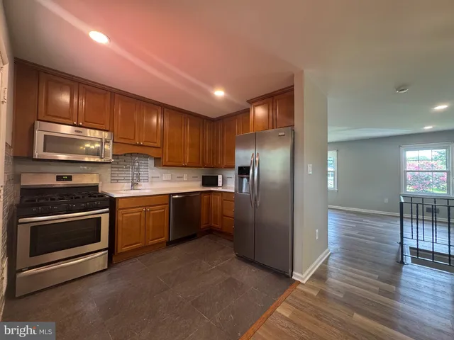 a kitchen with stainless steel appliances granite countertop a refrigerator a sink dishwasher a stove with wooden cabinets and floor