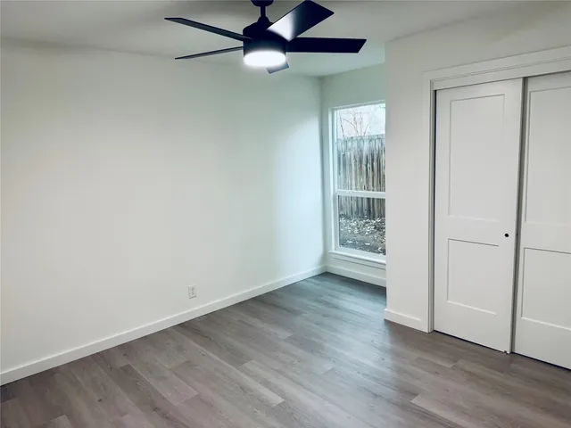 an empty room with wooden floor fan and windows