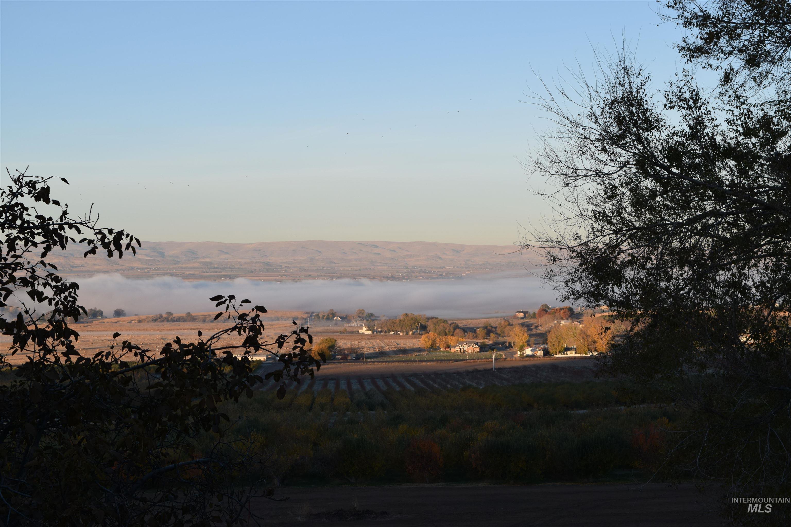 14526 Perfection Lane Caldwell, ID 83607 - Photo 5 of 47 Expansive rural landscape with distant hills, a low-lying fog bank, agricultural fields, and scattered residential structures