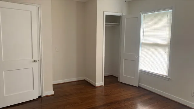 an empty room with wooden floor closet and windows