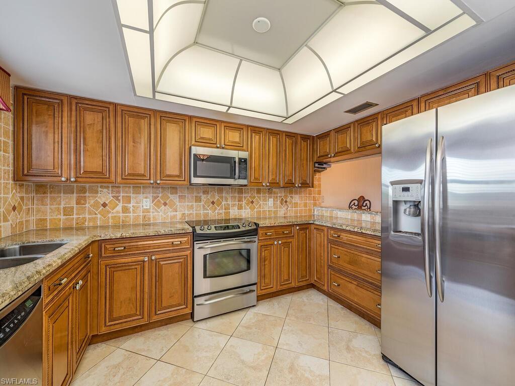 5590 Rattlesnake Hammock Road, Unit M203 Naples, FL 34113 - Photo 6 of 22 a kitchen with stainless steel appliances granite countertop a sink a stove a refrigerator a washer dryer and white cabinets