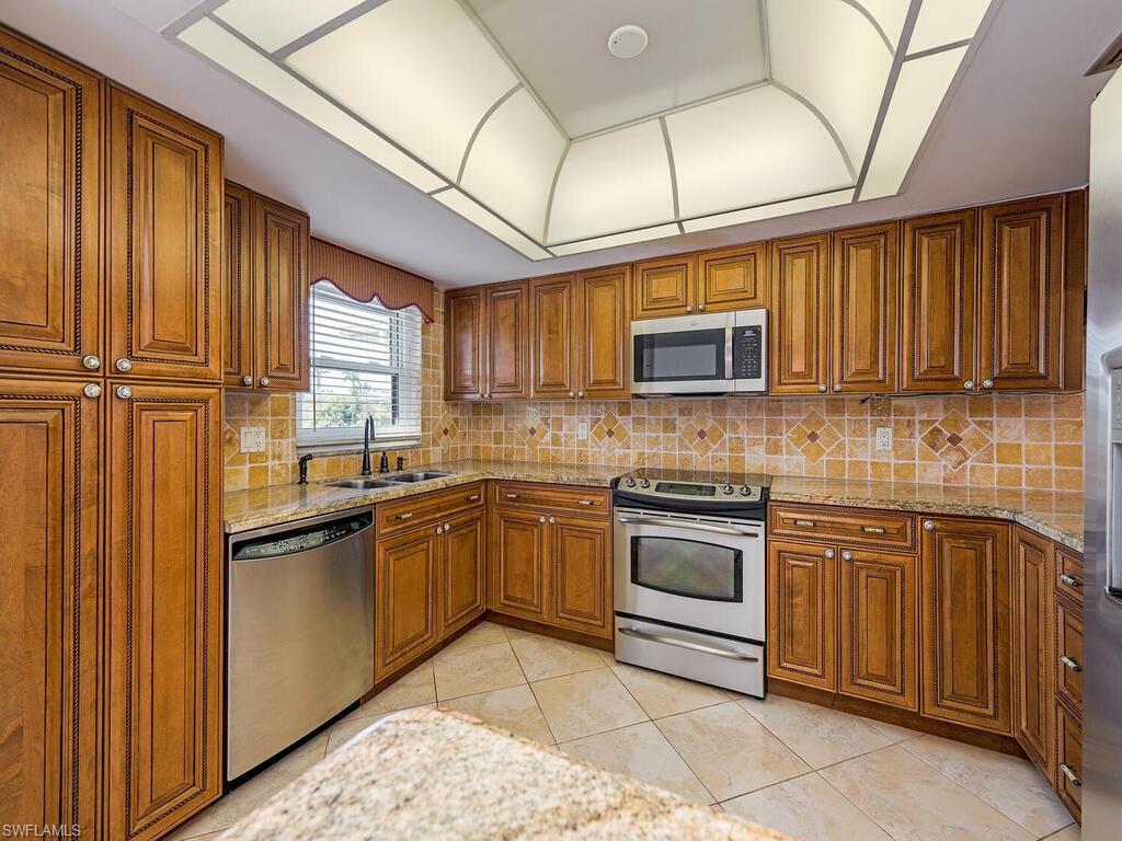 5590 Rattlesnake Hammock Road, Unit M203 Naples, FL 34113 - Photo 7 of 22 a kitchen with stainless steel appliances granite countertop wooden cabinets a sink and a stove