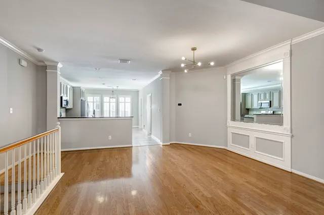 a view of an empty room and kitchen with wooden floor