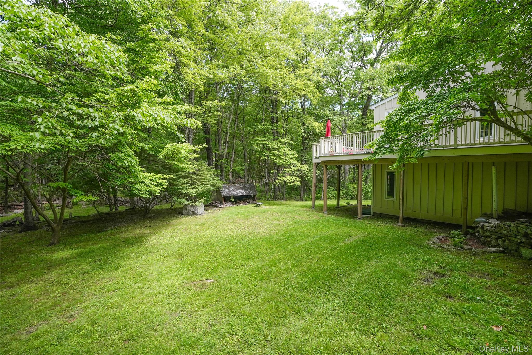 22 Peters Lane Pound Ridge, NY 10576 - Photo 40 of 43 Expansive green lawn surrounded by mature trees, featuring a raised outdoor deck with white railings
