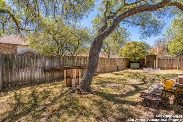 a backyard of a house with table and chairs with wooden fence and a large tree