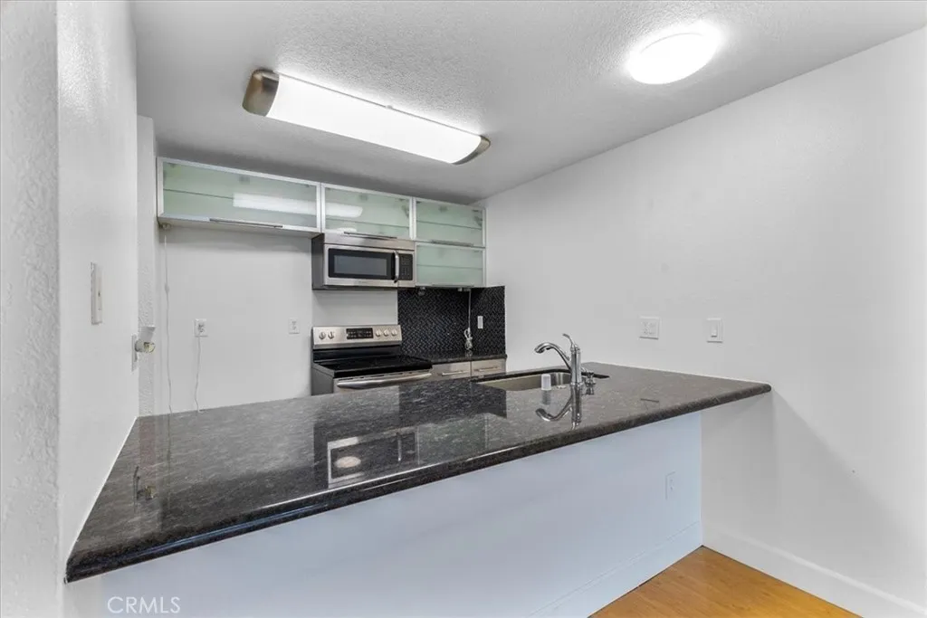 7890 East Spring Street, Unit 18F Long Beach, CA 90802 - Photo 5 of 31 a kitchen with stainless steel appliances granite countertop a sink a stove and a refrigerator with wooden floor