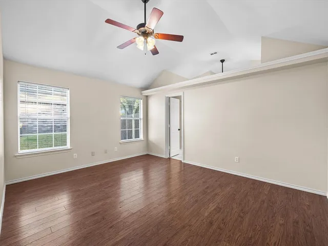 an empty room with wooden floor fan and windows