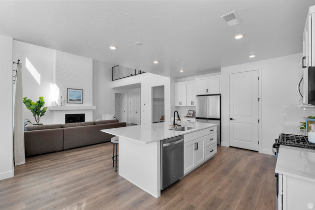 382 North Rhyolite Drive, Unit 111 Hurricane, UT 84737 - Photo 35 of 37 Open-concept living space featuring wood-finish flooring, a kitchen island with seating, white cabinetry with dark hardware, a stainless steel refrigerator, and a fireplace with a white mantel and shiplap accent wall