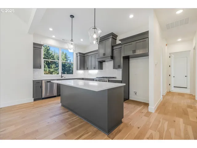 a large kitchen with stainless steel appliances kitchen island granite countertop a refrigerator a sink a stove and a wooden floors