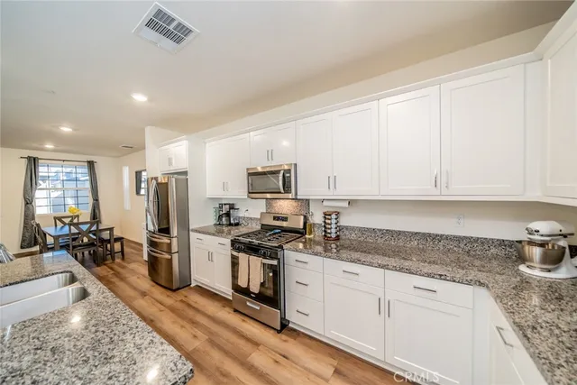 a kitchen with stainless steel appliances granite countertop a stove a sink a refrigerator white cabinets and couches with wooden floor