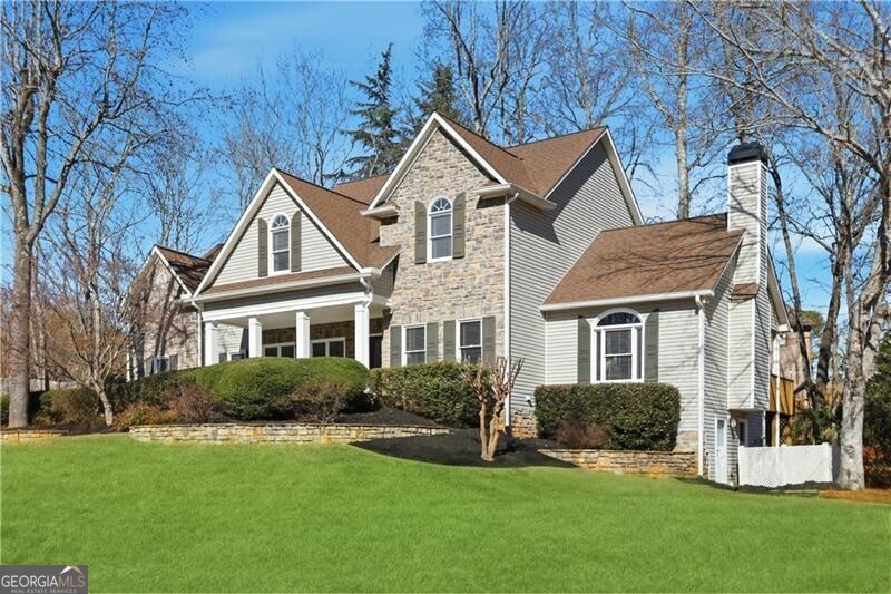 View of front of property featuring a front yard, a chimney, a shingled roof, and covered porch