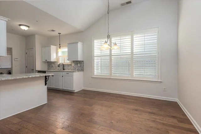 a large white kitchen with granite countertop a stove a sink a refrigerator and white cabinets with wooden floor