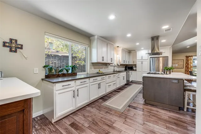 a kitchen with stainless steel appliances granite countertop a sink a stove a refrigerator cabinets and a dining table with wooden floor