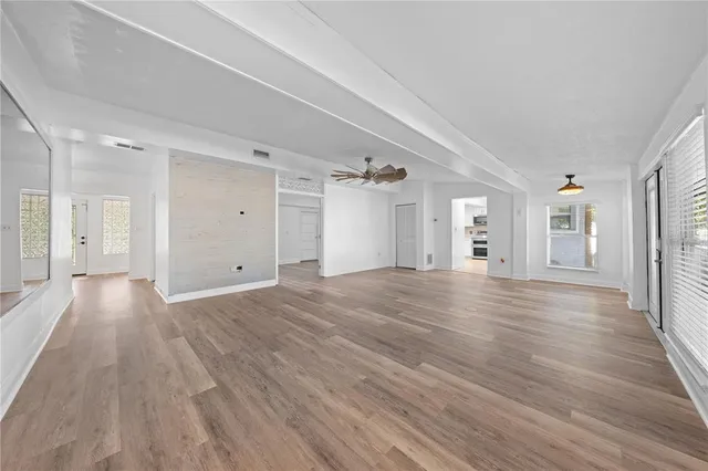 an empty room with wooden floor chandelier fan and windows