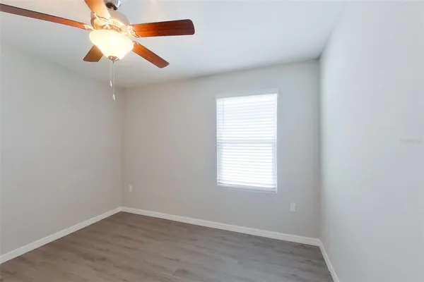 an empty room with wooden floor ceiling fan and window
