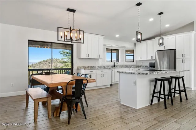 a kitchen with stainless steel appliances granite countertop a stove a refrigerator a kitchen island a sink a dining table and chairs with wooden floor