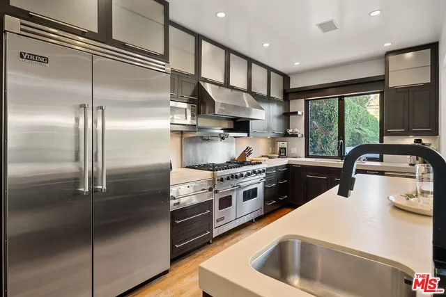 a kitchen with stainless steel appliances granite countertop a refrigerator a sink dishwasher a stove and a dining table with wooden floor