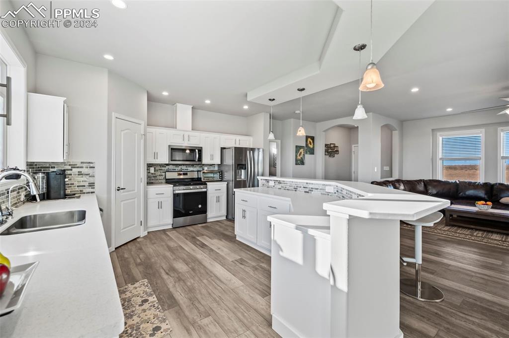 9393 North Log Road Calhan, CO 80808 - Photo 11 of 49 a kitchen with kitchen island a stove a sink a refrigerator and white cabinets with wooden floor