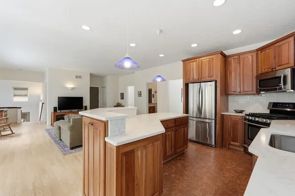 a large kitchen with stainless steel appliances kitchen island granite countertop a refrigerator a stove top oven a sink dishwasher and white cabinets with wooden floor