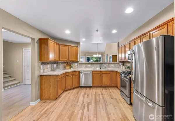 a kitchen with stainless steel appliances granite countertop a refrigerator oven a sink dishwasher and a stove with wooden floor