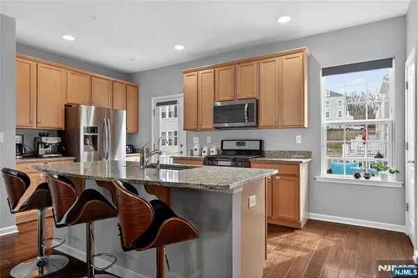 a kitchen with stainless steel appliances granite countertop a stove top oven a refrigerator a sink and a microwave with wooden floor