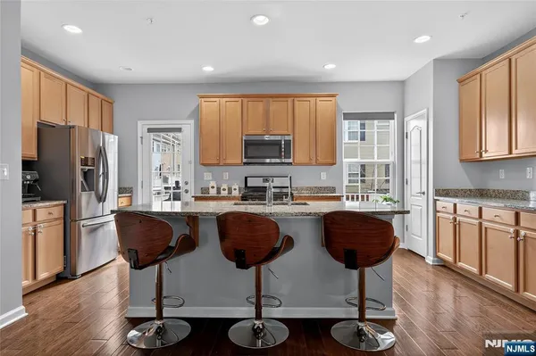 a kitchen with stainless steel appliances granite countertop a refrigerator a stove a sink cabinets and a dining table with wooden floor
