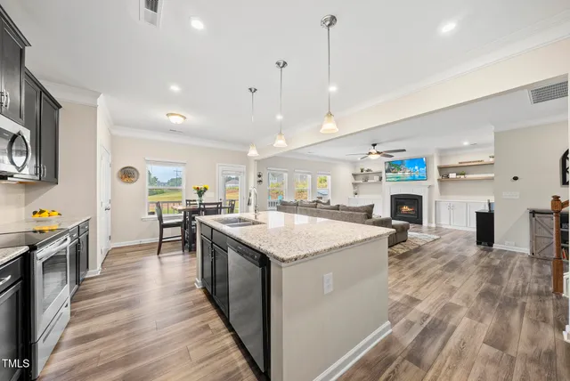 a kitchen with stainless steel appliances kitchen island granite countertop a stove top oven a sink a dining table and chairs with wooden floor