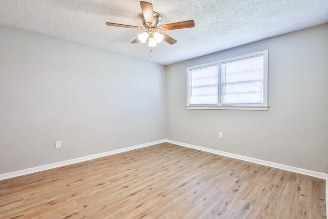 an empty room with wooden floor and a ceiling fan
