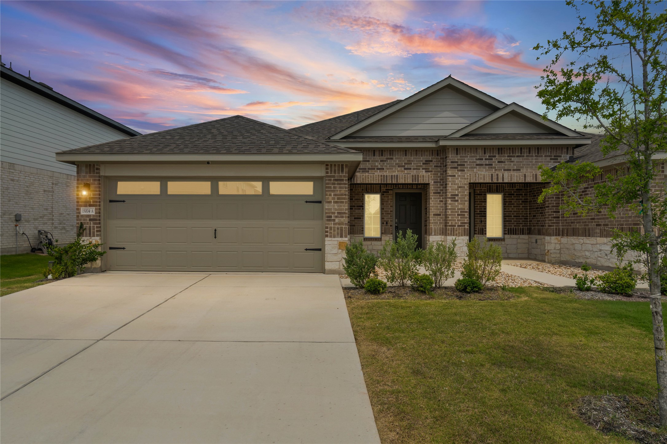 Brick exterior featuring a gabled roofline, an attached garage with upper window panels, and a concrete driveway