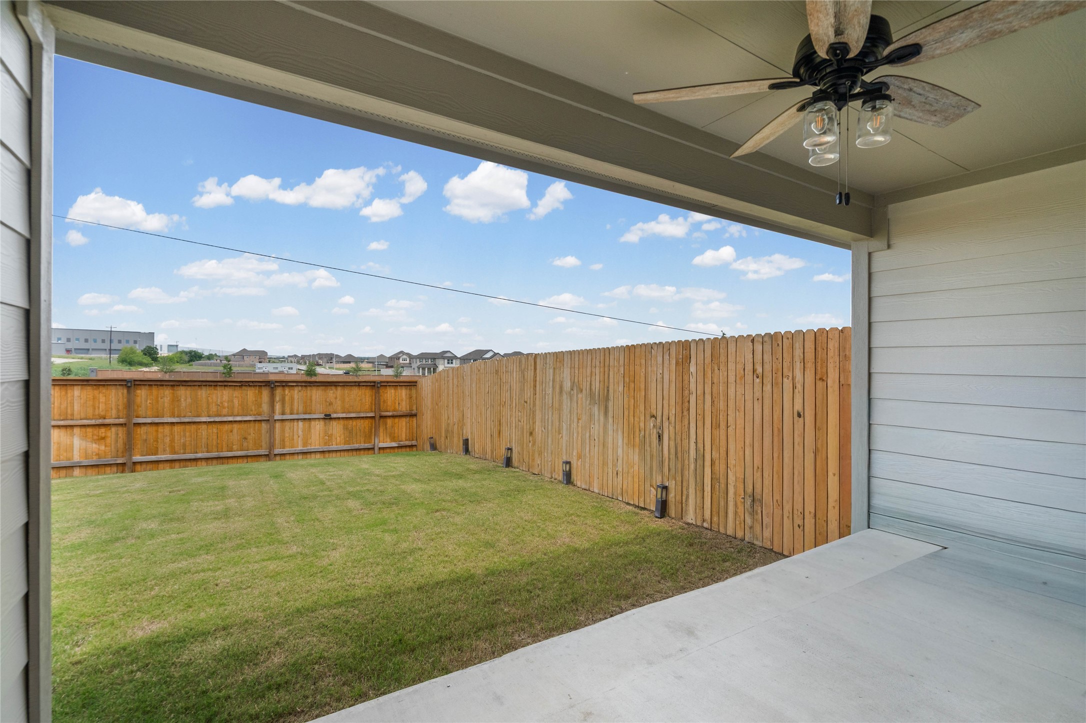 15004 Welsh Cobb Rd Manor, Unit A Manor, TX 78653 - Photo 17 of 22 Covered concrete patio featuring a ceiling fan with integrated lighting, overlooking a green lawn with a wood plank fence