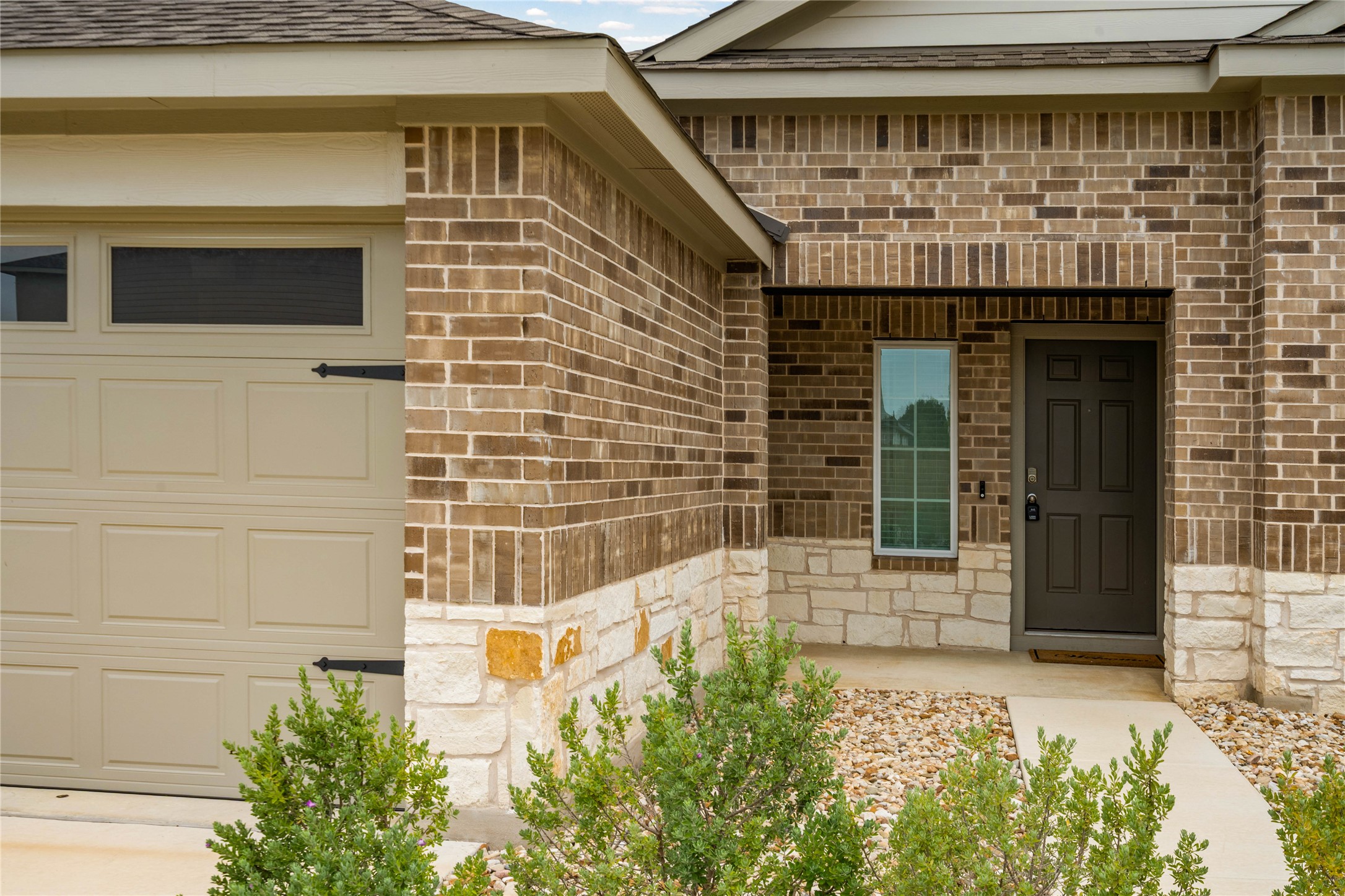 15004 Welsh Cobb Rd Manor, Unit A Manor, TX 78653 - Photo 3 of 22 Exterior featuring brick and stone veneer, an integrated garage with decorative hardware, a covered entry, and a paneled entry door