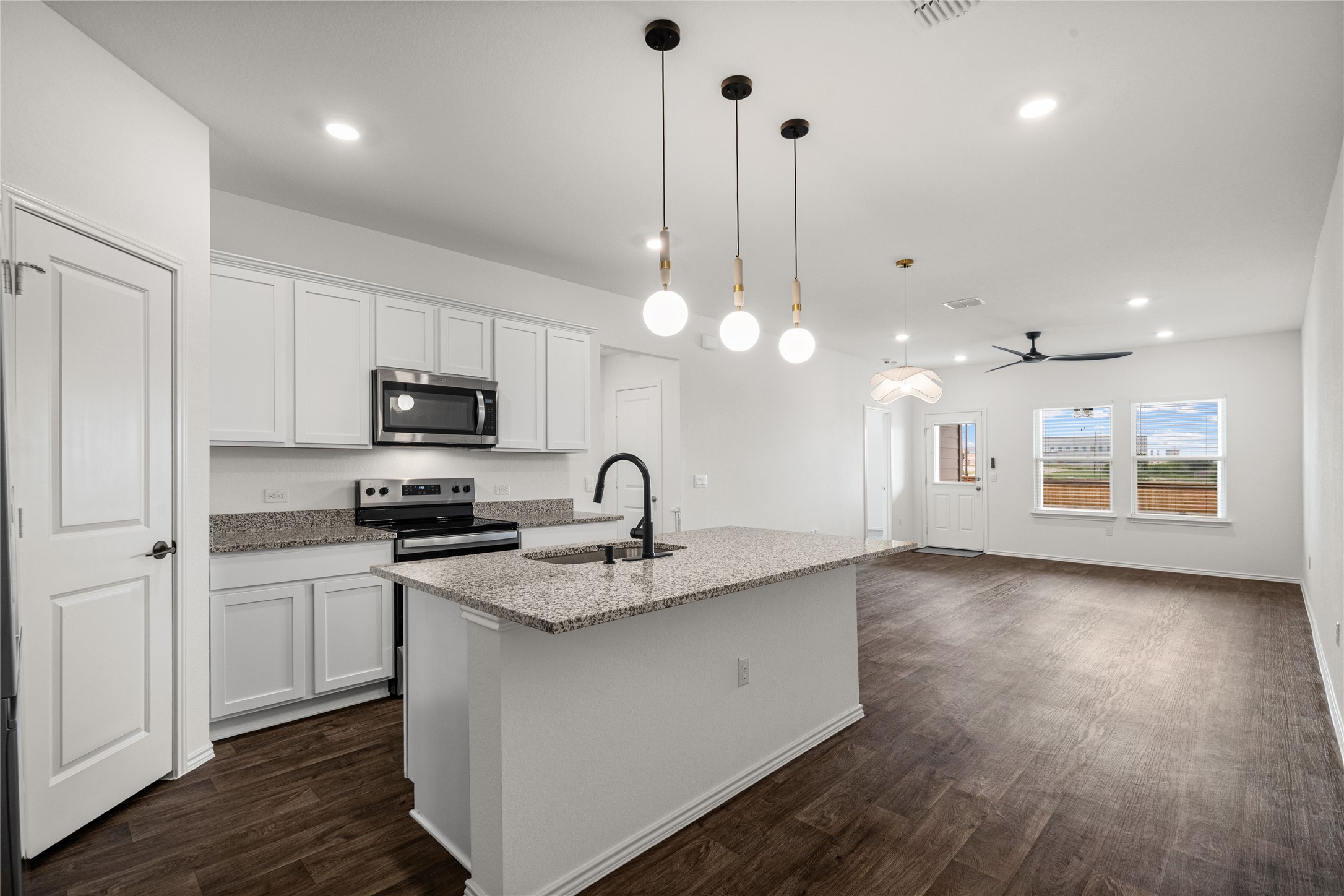 15004 Welsh Cobb Rd Manor, Unit A Manor, TX 78653 - Photo 6 of 22 Open-concept living area featuring a kitchen island with a granite-style countertop, stainless steel appliances, dark wood-finish flooring, and ample natural light from multiple windows