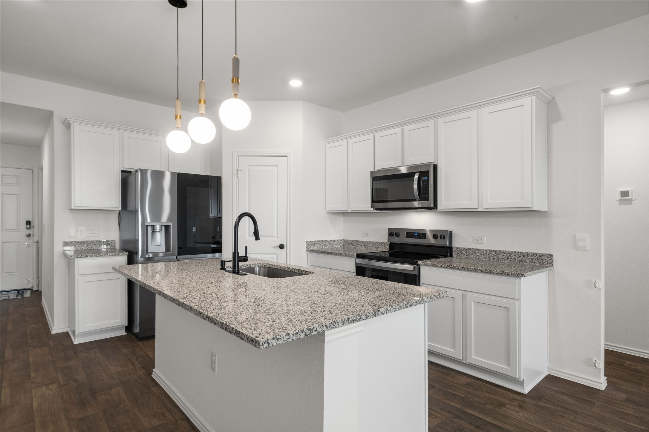15004 Welsh Cobb Rd Manor, Unit A Manor, TX 78653 - Photo 7 of 22 Kitchen featuring a central island with an integrated sink and matte black faucet, granite countertops, white cabinetry, stainless steel appliances, and wood-finish flooring