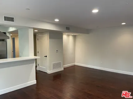 a view of an empty room with wooden floor and a bathroom