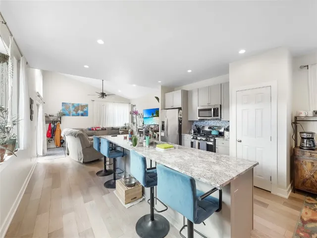 a kitchen with stainless steel appliances kitchen island granite countertop a dining table chairs and refrigerator